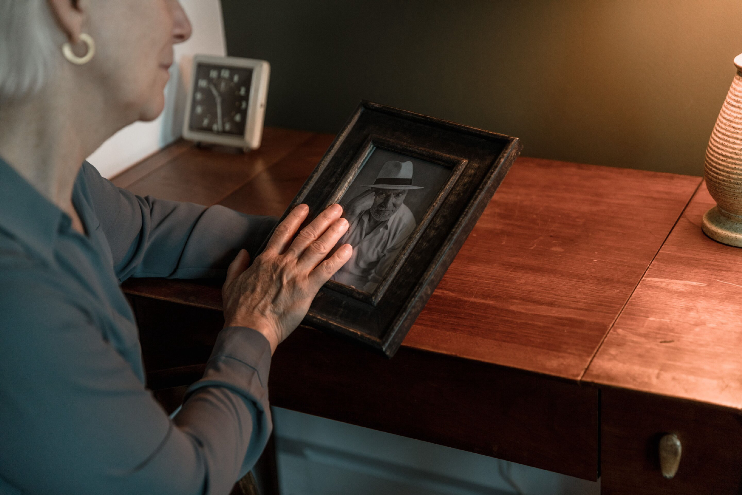 A person rests their hands on a framed black and white photograph sitting on a wooden desk.