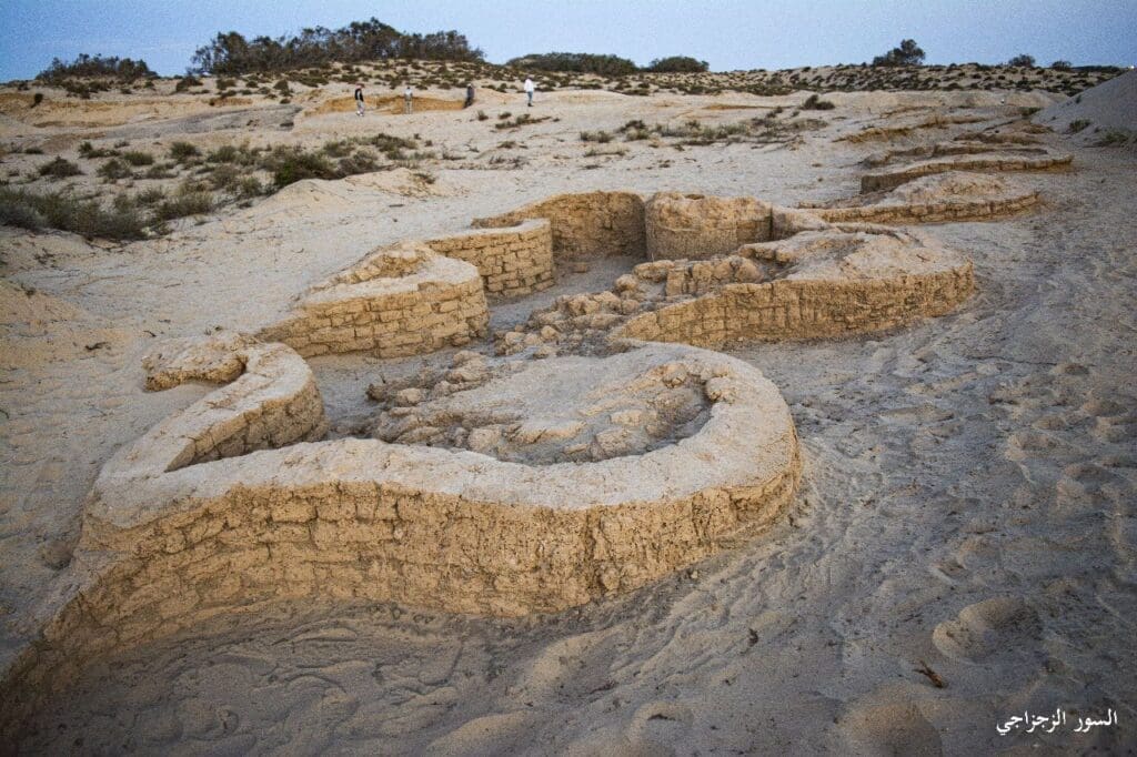 Low stone walls and foundations are partially buried in a sandy desert landscape.