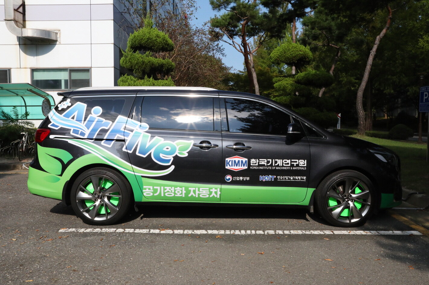A black minivan with green and blue graphics and text on its side is parked on a street.
